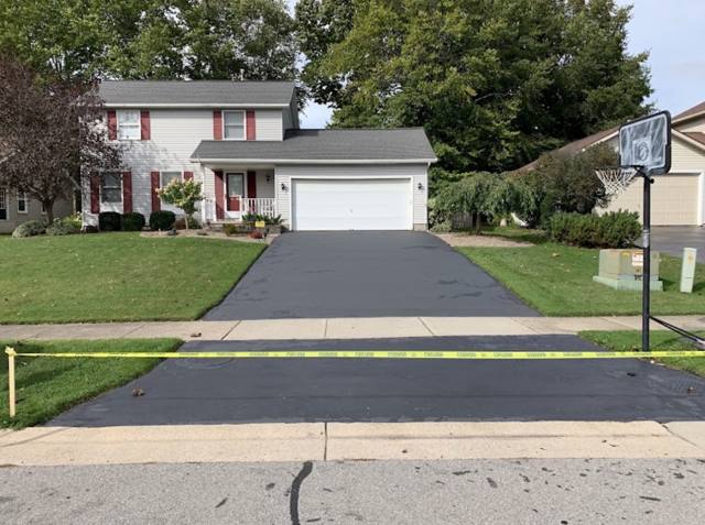 Freshly sealcoated driveway at a home with red shutters