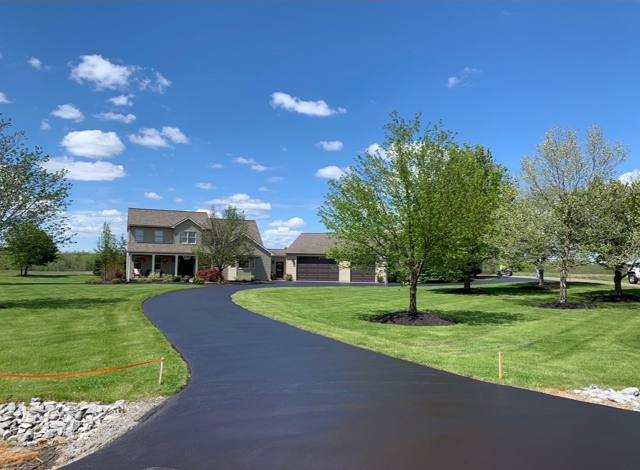 Glossy sealcoated curved driveway leading to a two-story country home