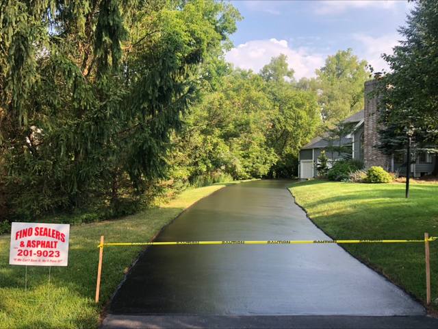 Long tree-lined driveway freshly sealcoated, with a Fino Sealers yard sign